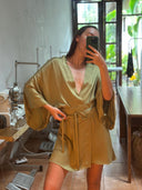 A woman takes a mirror selfie wearing the Rimmba | Sustainable Clothing Bunga Kimono in Mint Green, a belted mulberry silk robe dress with wide sleeves. Sewing machines and large windows with greenery are visible behind her.
