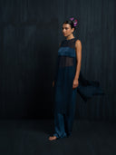 Barefoot woman wearing an indigo silk chiffon blouse and matching colour silk long pants against a dark background.