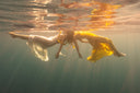 Two women are underwater posed wearing Mulberry silk dress white and yellow.  Hancrafted botanical-dyed sustainable luxury fashion for forma and resort wear.