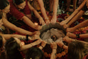 a group of people gathered closely in a circle around a large pot placed at the center. Their hands are extended toward the pot in a collective, symbolic gesture, creating a sense of unity and shared energy.