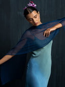 Close-up of woman wearing luxury ombre silk maxy dress and indigo scarf against a dark background.