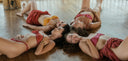 Four women in colorful pieces from Rimmba | Sustainable Clothing’s Botanical Dye Lingerie Workshop (Copy) 1 lie together on a wooden floor, smiling and relaxed in natural light, radiating joyful Full Moon Weekend vibes.