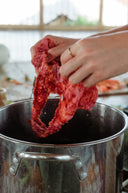 a person holding a piece of bright red fabric above a large metal pot. The fabric appears to be in the process of eco-printing activity.
