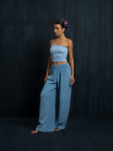 Barefoot woman wearing a baby indigo cotton strapless top and cotton long pants against a dark background.