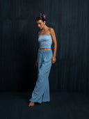 Barefoot woman wearing a baby indigo cotton strapless top and long pants cotton against a dark background.