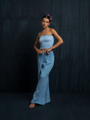 Woman wearing a baby indigo cotton strapless top and long cotton pants against a dark background.
