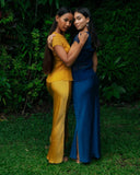 Two woman standing close together outdoors in a lush, green garden. They arer embracing each other gently, wih their arms around one another, creating a warm and intimate pose.