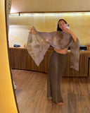 Karunia Fischer's posing for a mirror selfie in a RIMMBA Boutique. Cozy, warmly lit room with wooden flooring and modern interior decor. She is wearing a sophisticated earth-toned outfit consisting of a long, fittedMulberry silk aman bias skirt paired with a sheer Ecoprint scarf.