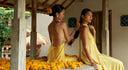 Two womans are sitting down on the wooden pavillion. They are both wearing Mulberry silk yellow dress with halter neck  and backless style.