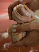 Two hands squeeze fabric bundles, showing orange and dark stains through the cloth over a reddish liquid during the Botanical Dye Lingerie Workshop by Rimmba | Sustainable Clothing.