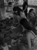 Women smile and craft with natural materials at the Botanical Dye Lingerie Workshop by Rimmba | Sustainable Clothing, gathered on woven mats in a bright space with lush greenery visible outside.