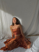 A woman in Rimmba | Sustainable Clothing’s Botanical Silk Dayu - Elastic Bandeau Top sits serenely on the floor, eyes closed and face upturned, framed by white drapes—a peaceful moment showcasing sustainable style.