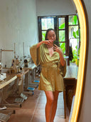 A woman wearing the Bunga Kimono in Mint Green by Rimmba | Sustainable Clothing takes a mirror selfie in a sewing studio with large windows, sewing machines, and plants in the background.