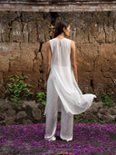 Back view of barefoot woman wearing White flared blouse and white silk pants wide leg. Hancrafted botanical-dyed  sustainable luxury fashion for bridal and resort wear.