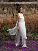 A barefoot woman wearing white silkchiffon blouse and white silk pants. Her background traditional clay wall and beautiful purple petals.