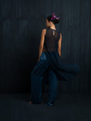 Barefoot woman wearing an indigo silk chiffon blouse and matching silk long pants is facing a dark background.