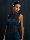 Woman wearing an indigo silk chiffon blouse and matching colour silk long pants against a dark background.