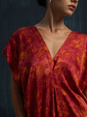 A woman poses against a dark background, wearing the Gaya Silk Kaftan Dress - Ecoprint Red by Rimmba | Sustainable Clothing. Only her lower face, neck, and upper torso are shown.