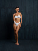 Woman wearing a white intimate set embroidery bra & underwear against a dark background.