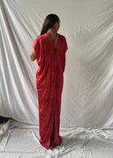 A person poses with their back to the camera in a Gaya Silk Kaftan Dress - Ecoprint Red by Rimmba | Sustainable Clothing. The dress showcases an elegant pattern, set against a white sheet backdrop and matching floor.