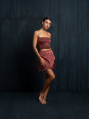 Barefoot woman wearing a red ecoprint silk strapless top and mini silk wrap skirt with a dark background.