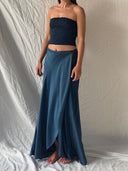 A woman stands barefoot on a light fabric backdrop, wearing the Indigo Silk Dayu - Elastic Bandeau Top by Rimmba | Sustainable Clothing and a matching indigo silk wrap skirt with a front slit. Her arms are relaxed at her sides; her head is out of frame.