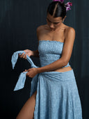 Woman wearing a baby indigo cotton embroidery strapless top and is tying the wrap skirt rope with a dark background.