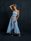 Barefoot woman wearing a baby indigo cotton embroidery strapless top and maxi wrap skirt with  a dark background.