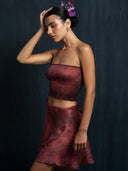Woman wearing a red ecoprint silk strapless top and mini silk wrap skirt with a dark background.