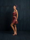Barefoot woman wearing a red ecoprint silk strapless top and mini silk wrap skirt with a dark background.