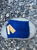 The Deep Blue - Indigo silk scarf by Rimmba | Sustainable Clothing, made from Mulberry Silk and natural plant dyes, is neatly folded on a large gray stone, surrounded by small rounded pebbles.