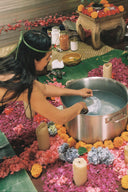 During RIMMBA's Botanical and Natural Dye Lingerie Workshop in Bali, a woman is performing a dyeing ritual with a pot surrounded by flowers and candles.