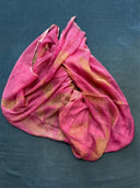 The Eco-Print Silk Chiffon Scarf in Bright Baby Pink by Rimmba | Sustainable Clothing, with sheer mulberry silk and gold accents, is displayed on a textured blue surface.