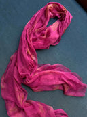 The Eco-Print Silk Chiffon Scarf - Fuchsia Pink by Rimmba | Sustainable Clothing, a lightweight magenta silk scarf with subtle yellow botanical prints, is displayed on a blue-grey fabric surface.