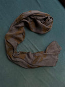 The Eco-Print Silk Chiffon Scarf - Grey by Rimmba | Sustainable Clothing, featuring botanical prints, is styled in a "C" shape against teal fabric.