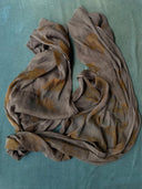 The Eco-Print Silk Chiffon Scarf - Grey by Rimmba | Sustainable Clothing, featuring unique botanical stains, is displayed on a turquoise textured surface. The scarf looks soft, sheer, and forms loose wavy folds.