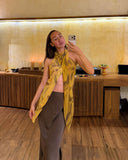 Karunia Fischer's taking a mirror selfie in RIMMBA store. She is wearing a stylish outfit consisting of a light-colored top, a fitted gray skirt, and a bright yellow scarf draped around her neck that hangs down in front.