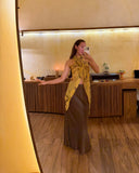 Karunia Fischer's taking a mirror selfie in RIMMBA store. She is wearing a stylish outfit consisting of a light-colored top, a fitted gray skirt, and a bright yellow scarf draped around her neck that hangs down in front.