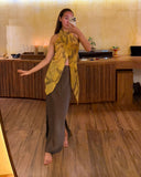 Karunia Fischer's taking a mirror selfie in RIMMBA store. She is wearing a stylish outfit consisting of a light-colored top, a fitted gray skirt, and a bright yellow scarf draped around her neck that hangs down in front.