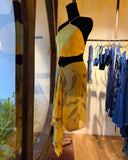 a mannequin dressed in a stylish outfit, positioned indoors near a doorway. The mannequin wearing a yellow halter silk top , paired with an ecoprint silkchiffon scarf marigold as a skirt. 
