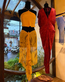Two mannequins displayed near a window. The left mannequin wearing Pevita halter top yellow, paired with an ecoprint silkchiffon scarf marigold. The right mannequin wearing Gaya kaftan silk red ecoprint.