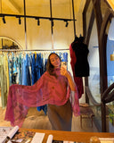 Karunia Fischer's  taking a mirror selfie in RIMMBA boutique. She is weraing Ecoprint scarf pink paired with fitted gray skirt. she is holding a smartphone in one hand while slightly posing, extending her sleeve to show its shape and fabric.