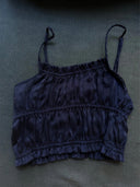 The Frida Crinkle Crop-Top by Rimmba | Sustainable Clothing, made from 100% Mulberry Silk with adjustable spaghetti straps and ruched fabric, is shown in navy blue lying flat on a dark surface.