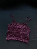 The Frida Crinkle Crop-Top by Rimmba | Sustainable Clothing, made from 100% Mulberry Silk, showcases a purple ruched design with spaghetti straps and is displayed flat on a dark fabric background.