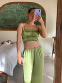 A woman in a Frida Crinkle Crop-Top by Rimmba | Sustainable Clothing takes a mirror selfie in a bright room, with a calico cat lounging on the bed in the background.