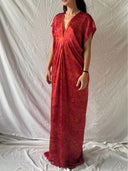 A woman poses before a white backdrop in the Gaya Silk Kaftan Dress - Ecoprint Red by Rimmba | Sustainable Clothing, a loose, floor-length style with subtle patterns and short sleeves. Her face is partially out of view.