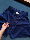A hand holds the Rimmba | Sustainable Clothing His & Hers Silk Bottoms - Boxers, featuring an elastic waistband, shown on a blue fabric surface.