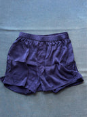 The His & Hers Silk Bottoms - Boxers from Rimmba | Sustainable Clothing, in navy blue natural-dyed silk with an elastic waistband, are laid flat on a blue fabric surface, showing a slightly wrinkled finish.