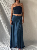 A woman stands before a cream backdrop wearing the Rimmba Indigo Silk Dayu Elastic Bandeau Top, her arms relaxed at her sides and feet bare.
