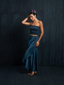 A woman wearing Jannah silk midi wrap skirt indigo and strapless top botanical dyed against a dark backround.